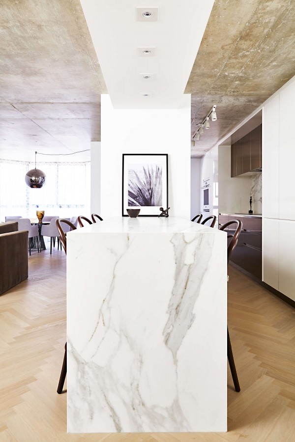 Kitchen with white marble waterfall island, wood counter stools, concrete ceiling, pot lights and herringbone wood flooring Kitchen with white marble waterfall island, wood counter stools, concrete ceiling, pot lights and herringbone wood flooring