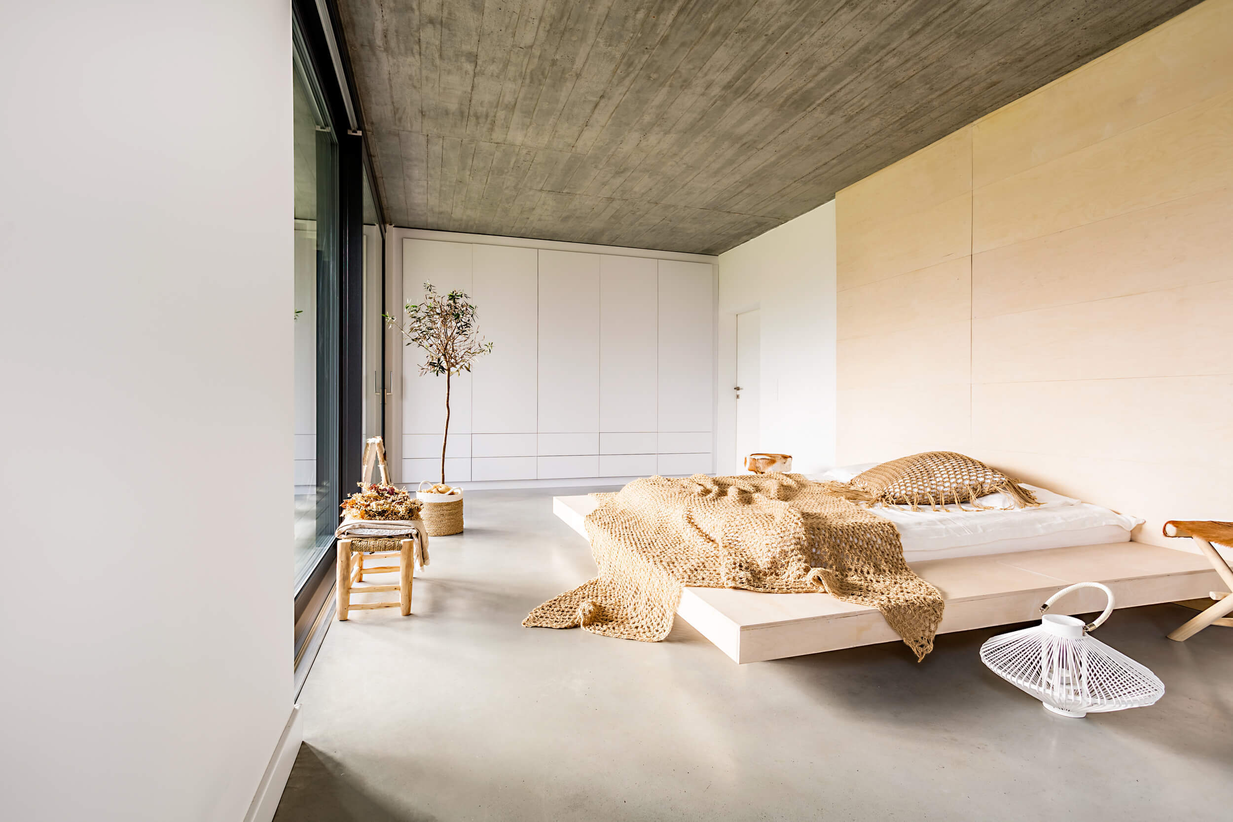 bedroom with white walls, wood ceiling, floating wood bed, wood bench, concrete floor, white lantern and white glossy storage cabinets