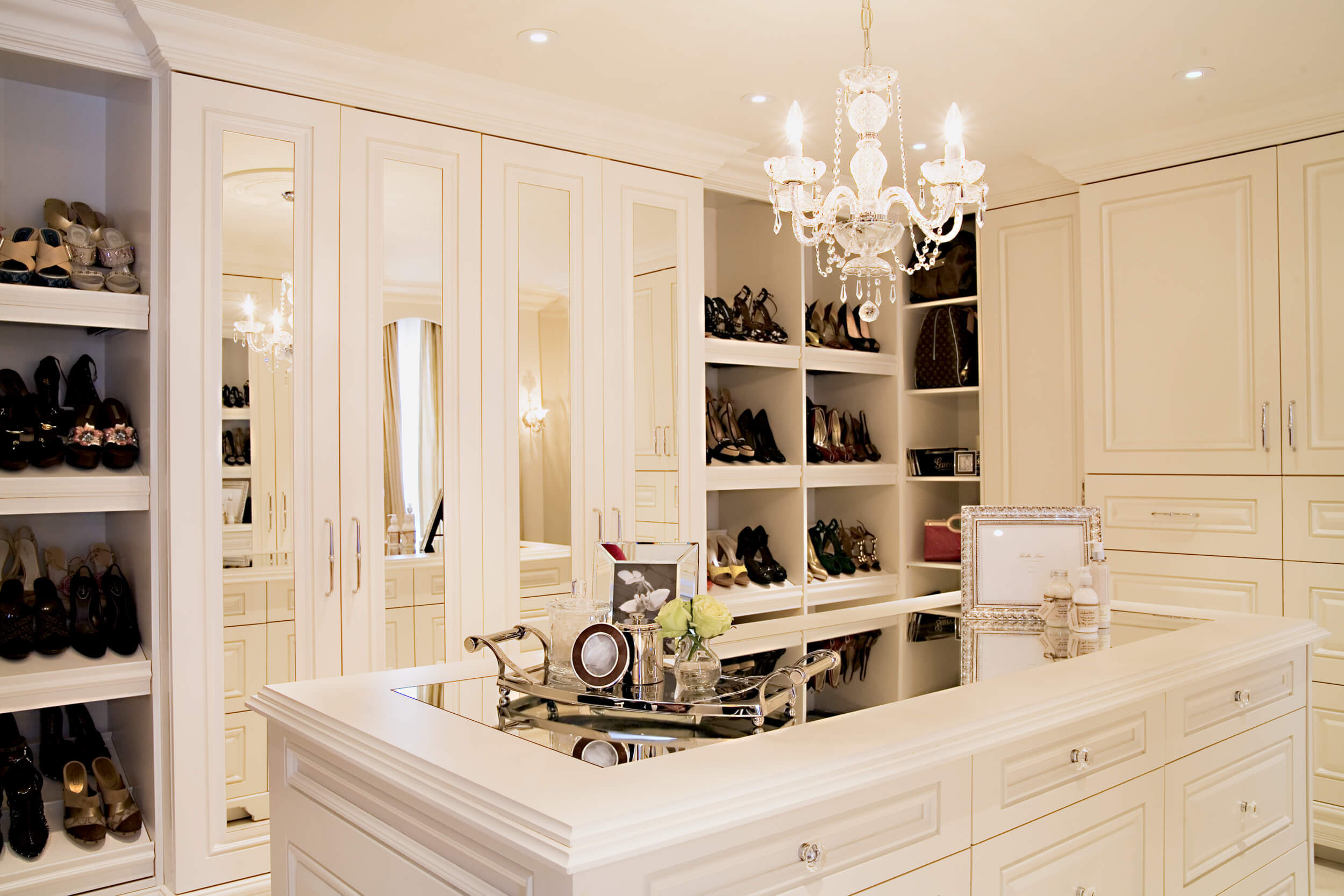 white wood walk in dressing room, crystal chandelier, mirror top island, mirrored doors and custom shelves for shoes