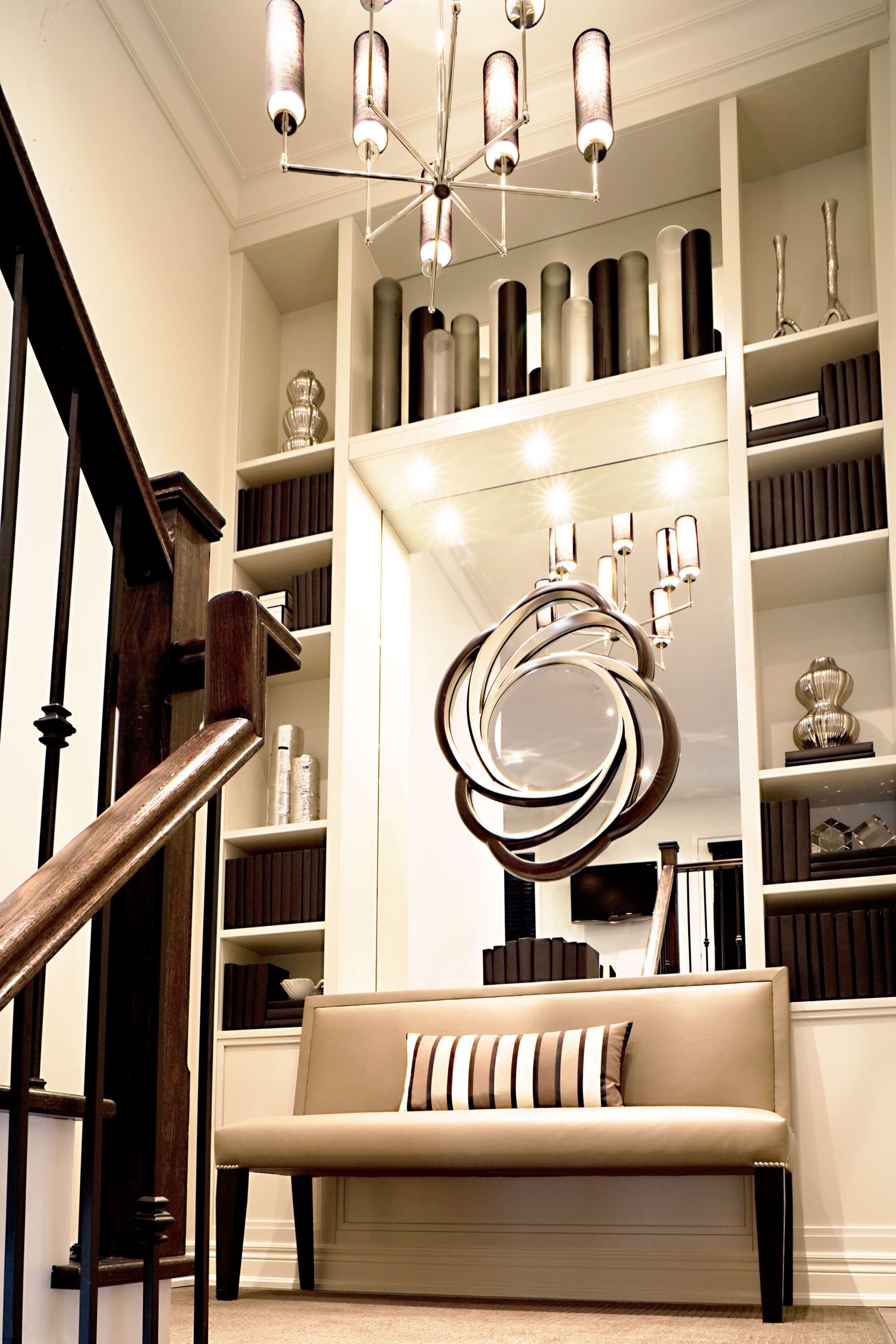 staircase landing with upholstered bench, striped accent pillow, custom shelving with built in mirror and large chandelier