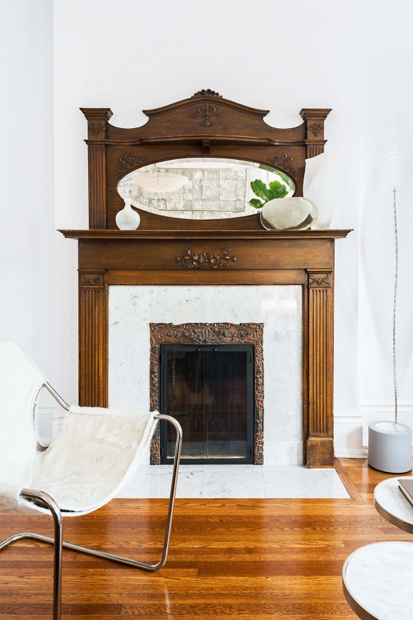 White marble Victorian wood fireplace, mantel mirror, hardwood floor, and white accent chair White marble Victorian wood fireplace, mantel mirror, hardwood floor, and white accent chair
