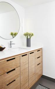 Limed oak blonde wood bathroom vanity with round mirror, white counter, undermount sink, chrome faucet, white sconce, and white walls and ceiling