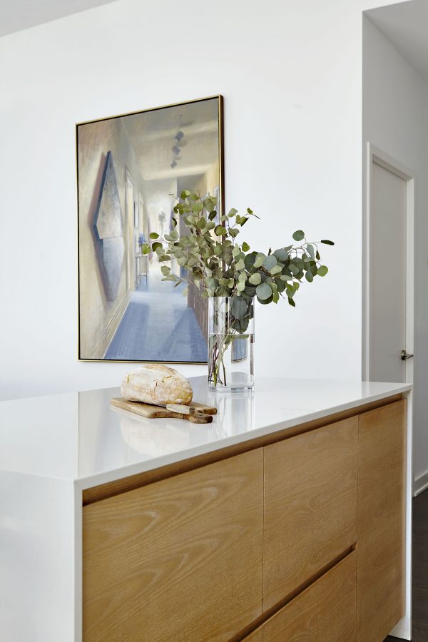 Custom kitchen waterfall island with white quartz countertop, limed oak cabinets, framed wall art and white walls Custom kitchen waterfall island with white quartz countertop, limed oak cabinets, framed wall art and white walls